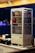 A beverage display fridge is filled with various drinks, including Pepsi, Coca-Cola, Mirinda, Lipton, and water bottles. It sits on a countertop with a cash register and a kettle nearby. The background is blurred with bokeh lights, indicating an indoor setting.