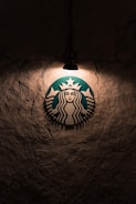 A logo featuring a mermaid with two tails is illuminated by a single overhead light against a textured, dark wall.