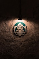 A logo featuring a mermaid with two tails is illuminated by a single overhead light against a textured, dark wall.