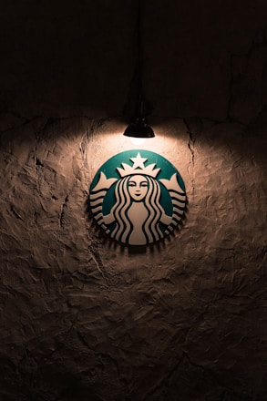 A logo featuring a mermaid with two tails is illuminated by a single overhead light against a textured, dark wall.