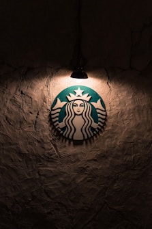 A logo featuring a mermaid with two tails is illuminated by a single overhead light against a textured, dark wall.