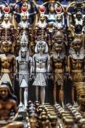 A collection of intricately designed Egyptian statues depicting ancient deities and pharaohs. The figures are dressed in traditional attire, adorned with headdresses and symbols of ancient Egyptian culture. The craftsmanship features detailed patterns and vibrant colors.