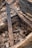 A collection of metal objects and debris are found among charred wooden beams and rubble. The scene appears to depict remnants of a burned or collapsed structure, with visible blackened wood and scattered stones.