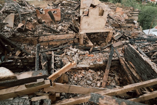 Burnt remains of a home with firefighters in the background.