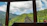 A cozy train cabin window framing lush green hills under a clear sky.
