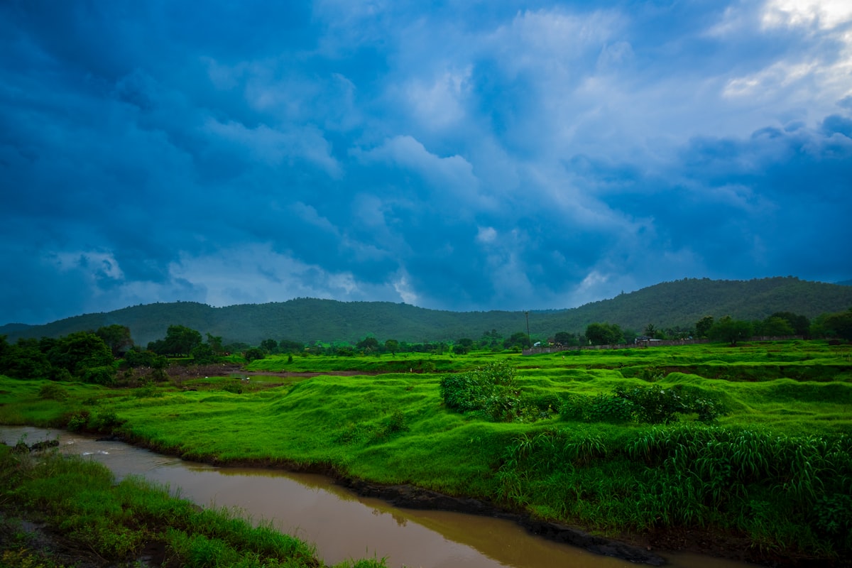 A turbulent river running through a lush green valley under heavy monsoon clouds