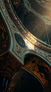 Elaborate architectural design featuring intricate patterns and ornate details, illuminated by a warm light source. The structure includes arches and decorative elements with a blend of dark and luminous tones.