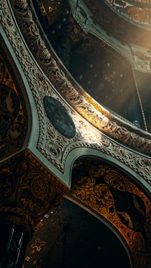 Elaborate architectural design featuring intricate patterns and ornate details, illuminated by a warm light source. The structure includes arches and decorative elements with a blend of dark and luminous tones.
