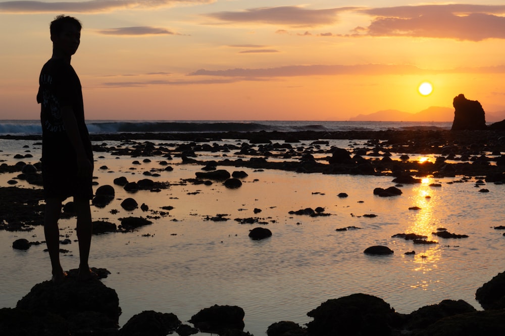 a man standing on a rocky beach at sunset