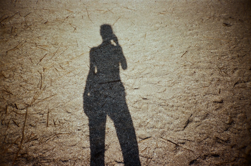 a shadow of a person standing in the dirt