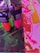 Several tubes of Liquitex Basics Acrylic paint stand on a colorful canvas. The colors include vibrant greens, pinks, and oranges. The canvas underneath features abstract, energetic brushstrokes in vivid pink, red, and orange hues, with some areas of dark green and black.