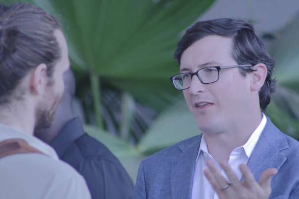 A mentor and mentee sharing a thoughtful conversation outdoors, with greenery in the background.