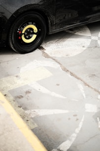A car with a yellow sticker marked '80' on the wheel is parked on a concrete surface with faded white and yellow markings.