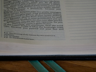 A close-up of an open book showing a passage of text on the left page. The text appears to be a passage from a religious or historical document with reference notations at the bottom of the page. The right margin features a series of dots for note-taking or annotation.