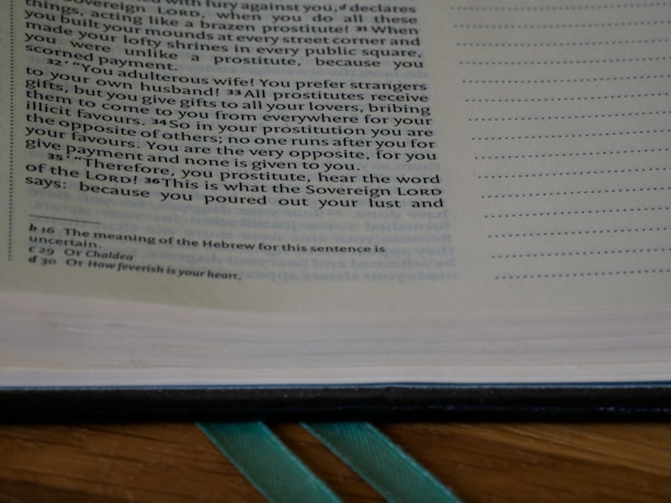 A close-up of an open book showing a passage of text on the left page. The text appears to be a passage from a religious or historical document with reference notations at the bottom of the page. The right margin features a series of dots for note-taking or annotation.