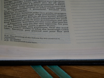 A close-up of an open book showing a passage of text on the left page. The text appears to be a passage from a religious or historical document with reference notations at the bottom of the page. The right margin features a series of dots for note-taking or annotation.