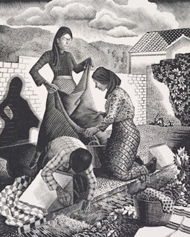 Three figures engaged in communal work outdoors. A woman in a long dress holds a large piece of fabric while another woman kneels, assisting with the fabric. A third person, bending over, works on the ground, surrounded by a basket and patterned textiles. The background shows trees, hills, a house, and a cloudy sky, creating a rural and serene setting.