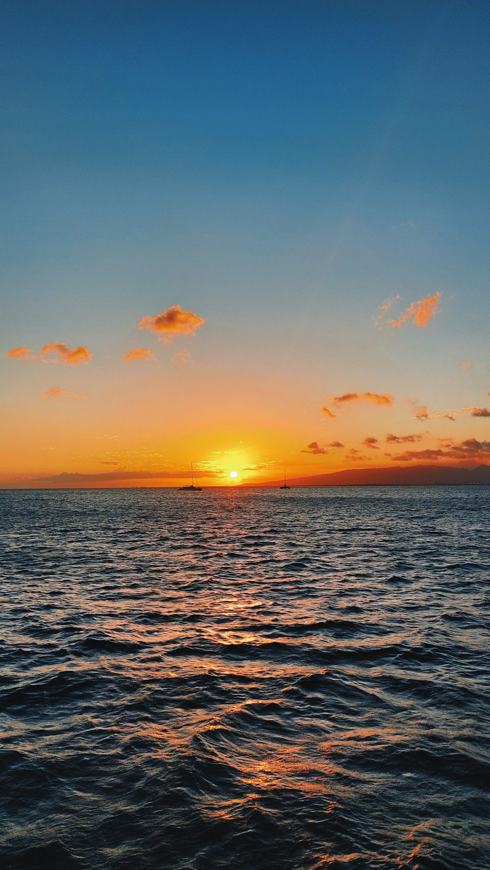 the sun is setting over the ocean with a boat in the distance