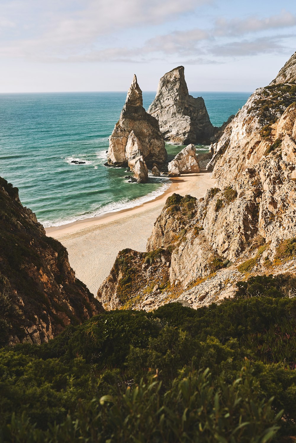 a sandy beach next to the ocean with rocks in the background