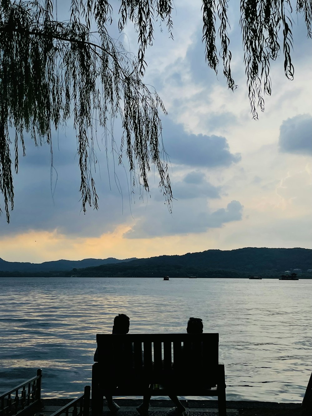 two people sitting on a bench near the water