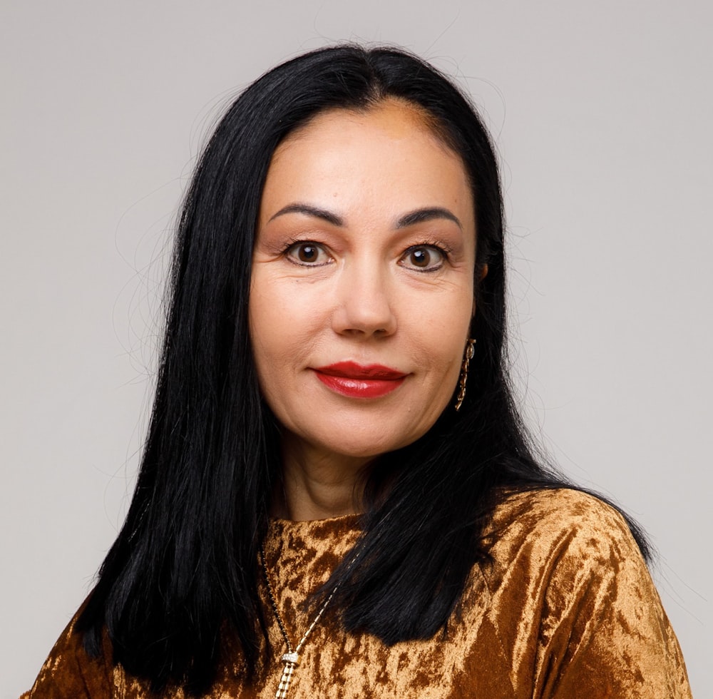 a woman with long black hair wearing a gold top