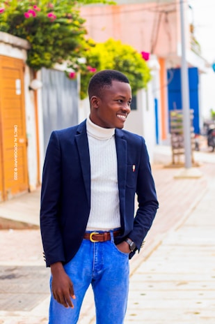 A stylish young man wearing a sleek navy blazer and white shirt, standing confidently against a minimalist urban backdrop.