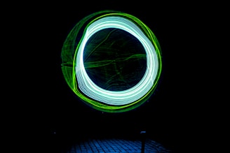 A dark background features a bright circle composed of intertwined neon blue and green light trails, creating a dynamic and futuristic effect.