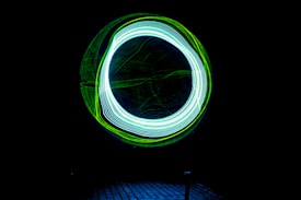 A dark background features a bright circle composed of intertwined neon blue and green light trails, creating a dynamic and futuristic effect.