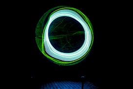 A dark background features a bright circle composed of intertwined neon blue and green light trails, creating a dynamic and futuristic effect.