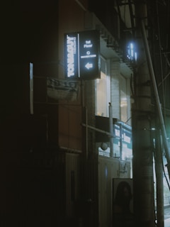 An urban street scene at night with illuminated signage for a hairdressing salon on the side of a building. The scene includes a dimly lit environment with a street light and cables.