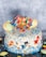 A decorated cake featuring superhero-themed edible figures and colorful candies. The cake is adorned with figures of various superheroes on top, surrounded by a sprinkle of blue and gold stars. Macarons in pastel colors are placed around the edges, complementing the vibrant color palette.