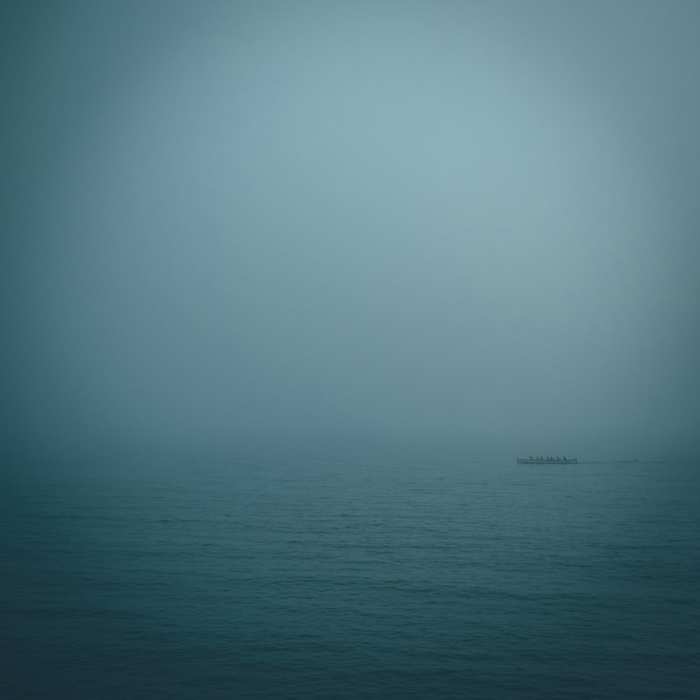 a lone boat in the middle of the ocean on a foggy day