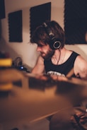 A person with headphones is engaged in playing a musical instrument in a studio setting. Soundproof panels are visible on the walls, suggesting an audio recording environment. The lighting is warm and soft, creating a focused and intimate atmosphere.