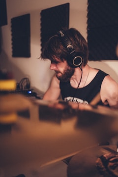 A person with headphones is engaged in playing a musical instrument in a studio setting. Soundproof panels are visible on the walls, suggesting an audio recording environment. The lighting is warm and soft, creating a focused and intimate atmosphere.