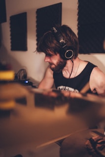 A person with headphones is engaged in playing a musical instrument in a studio setting. Soundproof panels are visible on the walls, suggesting an audio recording environment. The lighting is warm and soft, creating a focused and intimate atmosphere.