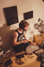 A curious boy wearing headphones, tapping a drum with enthusiasm.