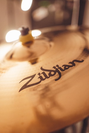 A close-up of a cymbal with the brand name 'Zildjian' clearly visible. The lighting creates soft reflections and highlights on the metallic surface, adding warmth and depth to the image.