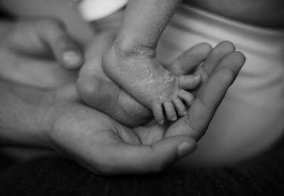 A close-up of an adult's hand gently cradling a newborn's foot, showing delicate textures and tenderness.