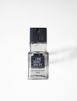 A clear glass bottle of Jacques Bogart eau de toilette with a dark grey cap. The label on the front reads 'ONE MAN SHOW' with additional details about the fragrance. The bottle casts a soft shadow on a white background.