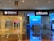 A hallway in a shopping mall features two bank outlets side by side: Bank of China (Hong Kong) on the left and Citibank on the right. Both banks have illuminated signs with their logos. The Bank of China section shows a closed office area with some ATMs in use by customers. The Citibank area has a bright, blue-lit interior with a welcoming entrance.