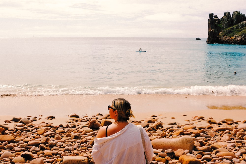 a woman sitting on a rocky beach next to the ocean