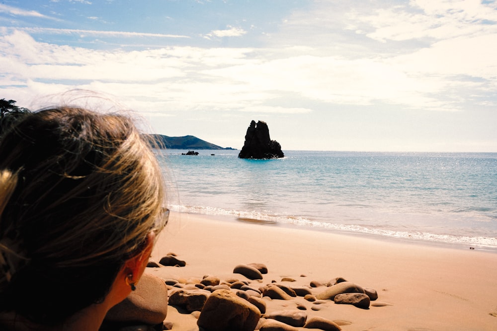 a woman sitting on a beach looking out at the ocean