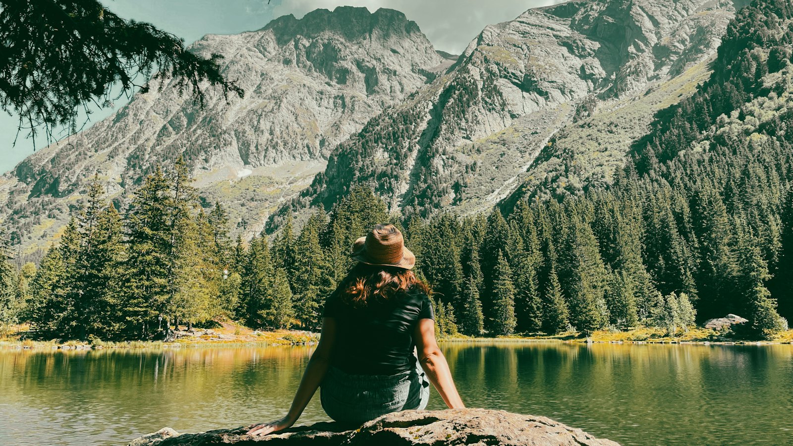 Woman seated in meditation on a rock beside a calm mountain lake