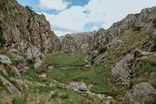 a grassy valley surrounded by rocky mountains under a cloudy sky