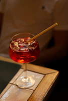 An elegant glass of cocktail with ice cubes reflecting neon red and white lights in a dark setting.