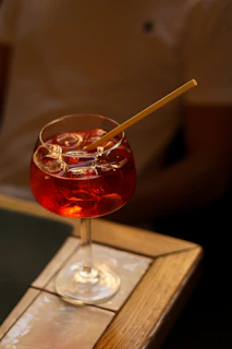 An elegant glass of cocktail with ice cubes reflecting neon red and white lights in a dark setting.