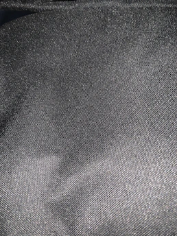 A close-up of a finely textured fabric in deep charcoal, illuminated softly to reveal subtle gold threads.