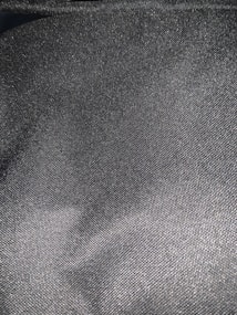 A close-up view of a textured, dark gray fabric with a visible weave pattern. The fabric appears to have a slight sheen, which reflects light subtly across its surface.