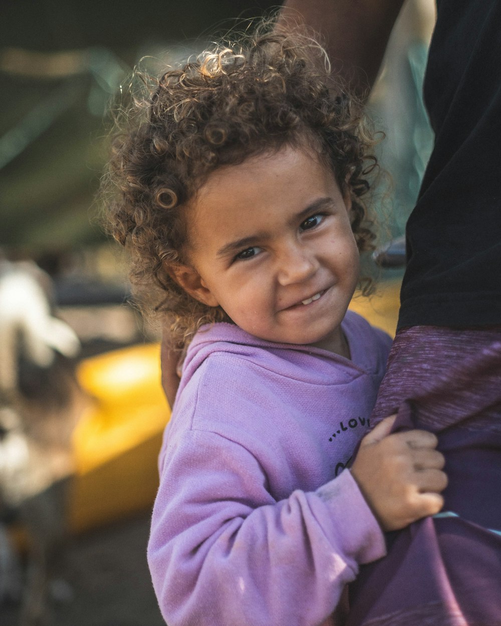 a little girl with curly hair holding onto a persons arm