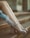 A pair of legs in sheer dotted socks and stylish high-heeled shoes are elegantly displayed on stone steps. The wearer also dons delicate gloves, adorned with a pearl ring, which adds a touch of vintage charm to the ensemble.